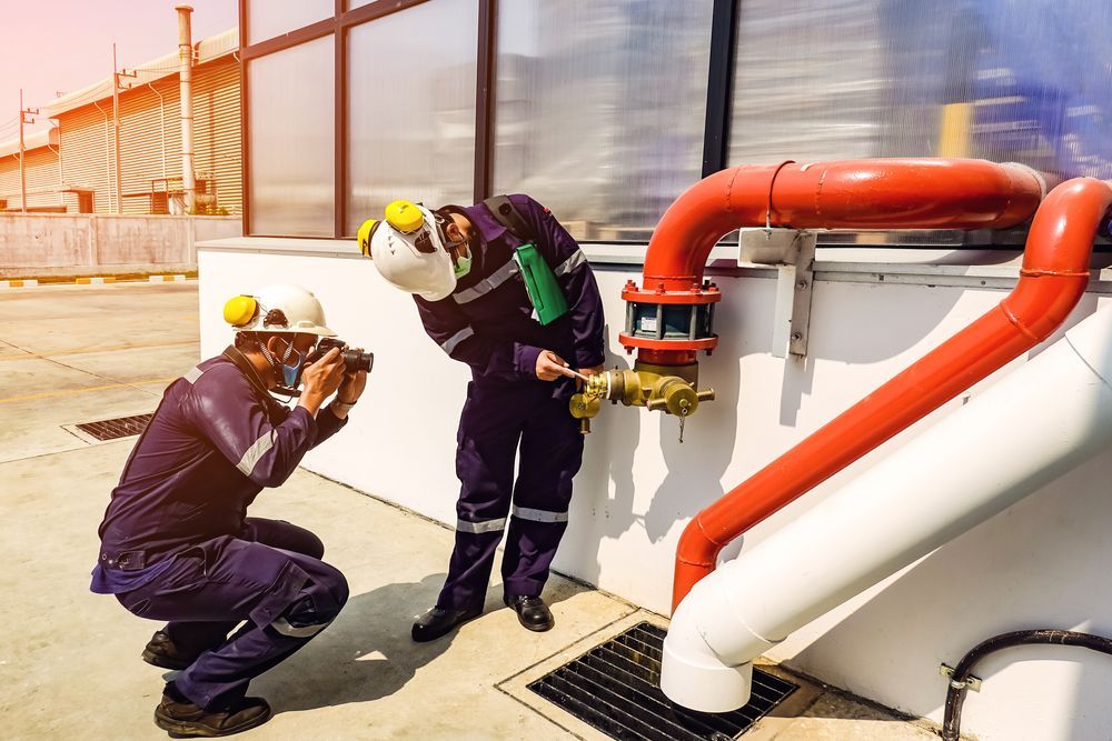 Two Workers Inspect Plumbing, One Taking a Photo — Hunter Fire & Safety in Edgeworth, NSW