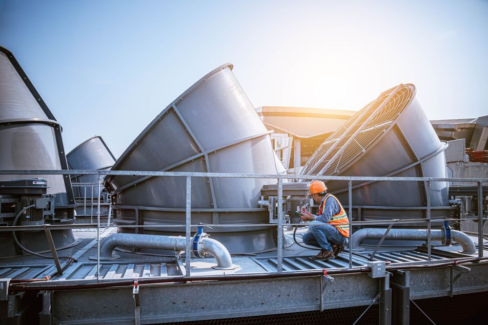 Man in Safety Vest Inspects Industrial Cooling Towers Under a Bright Sky — Hunter Fire & Safety in Coffs Harbour, NSW