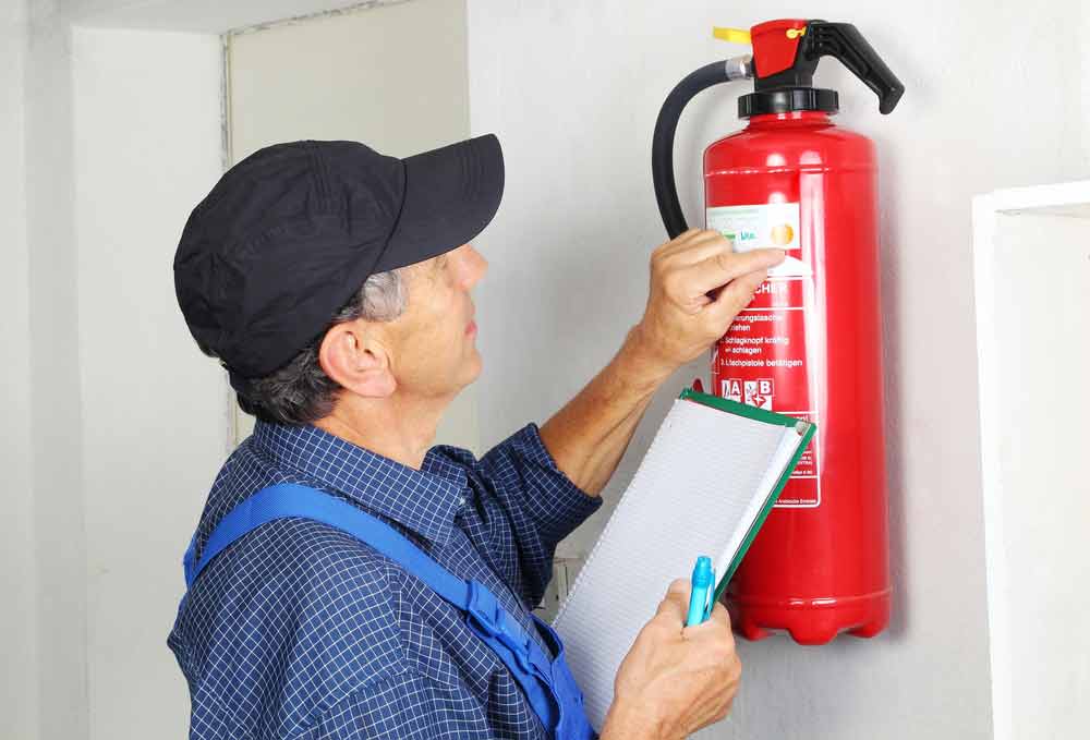 Person in Blue Overalls Inspecting a Red Fire Extinguisher — Hunter Fire & Safety in Edgeworth, NSW