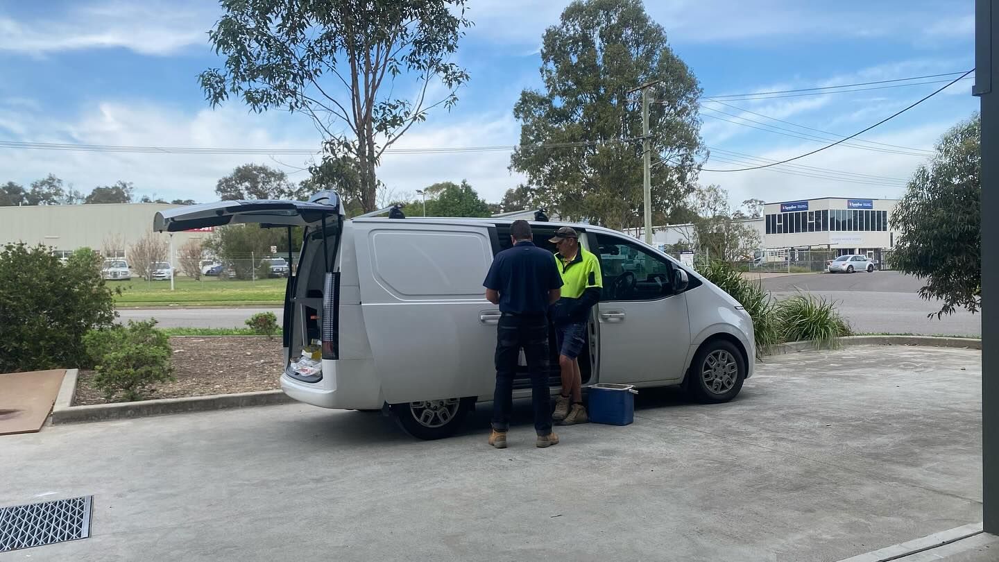 Two Men Loading a White Van Outdoors on a Cloudy Day — Hunter Fire & Safety in Newcastle, NSW