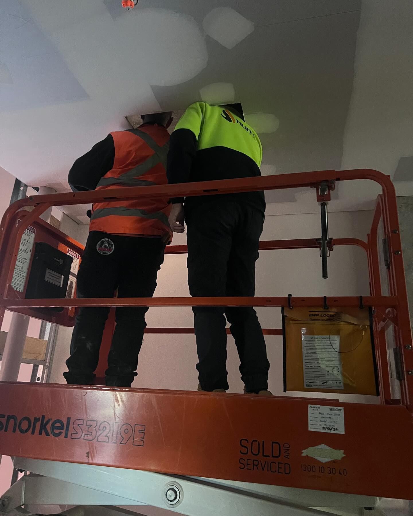 Two Workers on an Orange Lift Platform Repair a Ceiling — Hunter Fire & Safety in Edgeworth, NSW