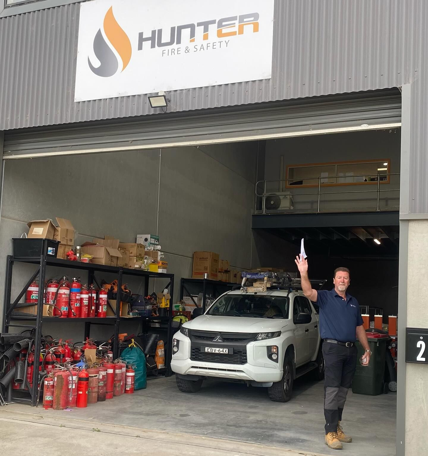 Man Waving in Front of a Warehouse Entrance With Hunter Fire & Safety Sign — Hunter Fire & Safety in Edgeworth, NSW