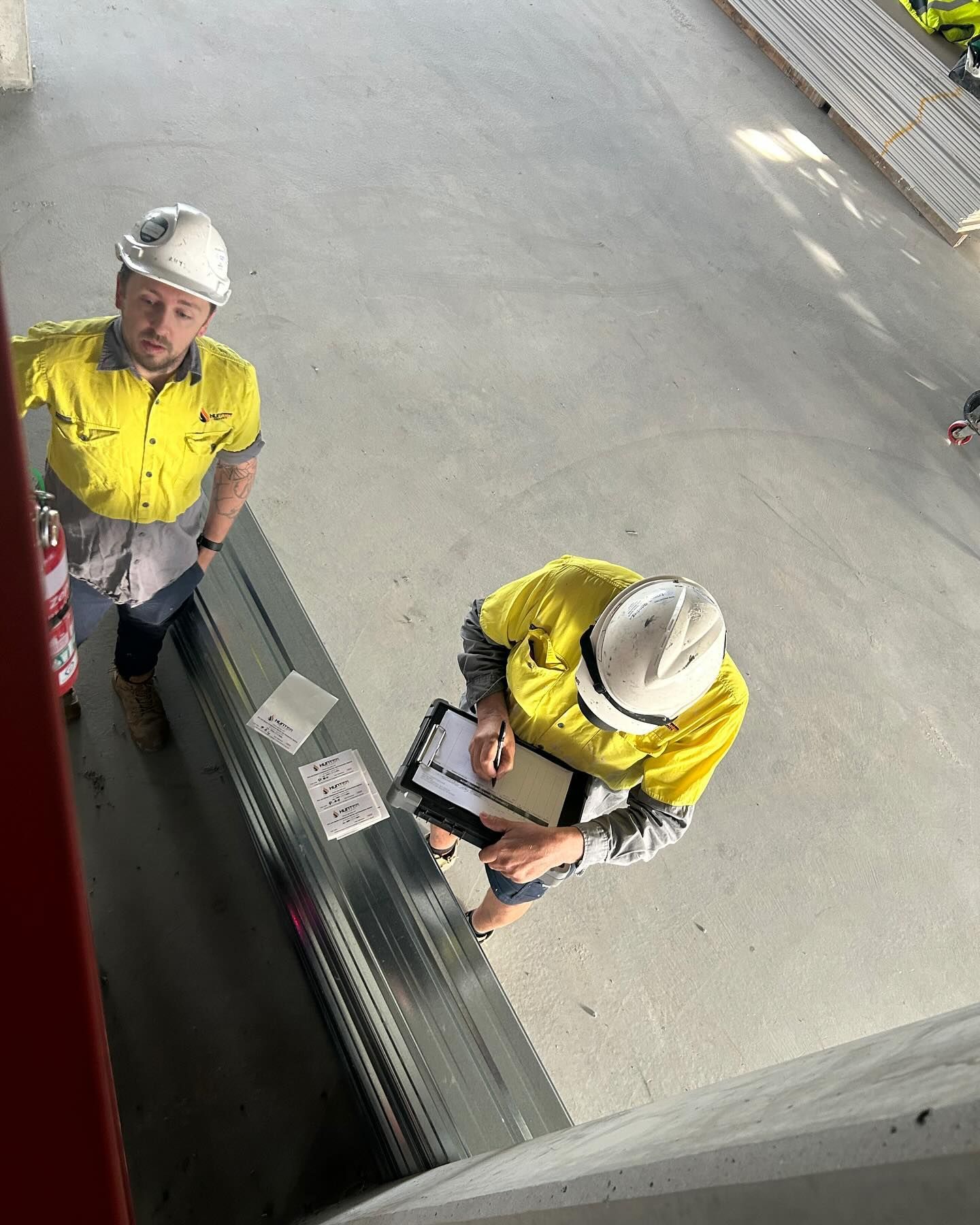 Two Construction Workers in Hard Hats Review Paperwork  — Hunter Fire & Safety in Edgeworth, NSW