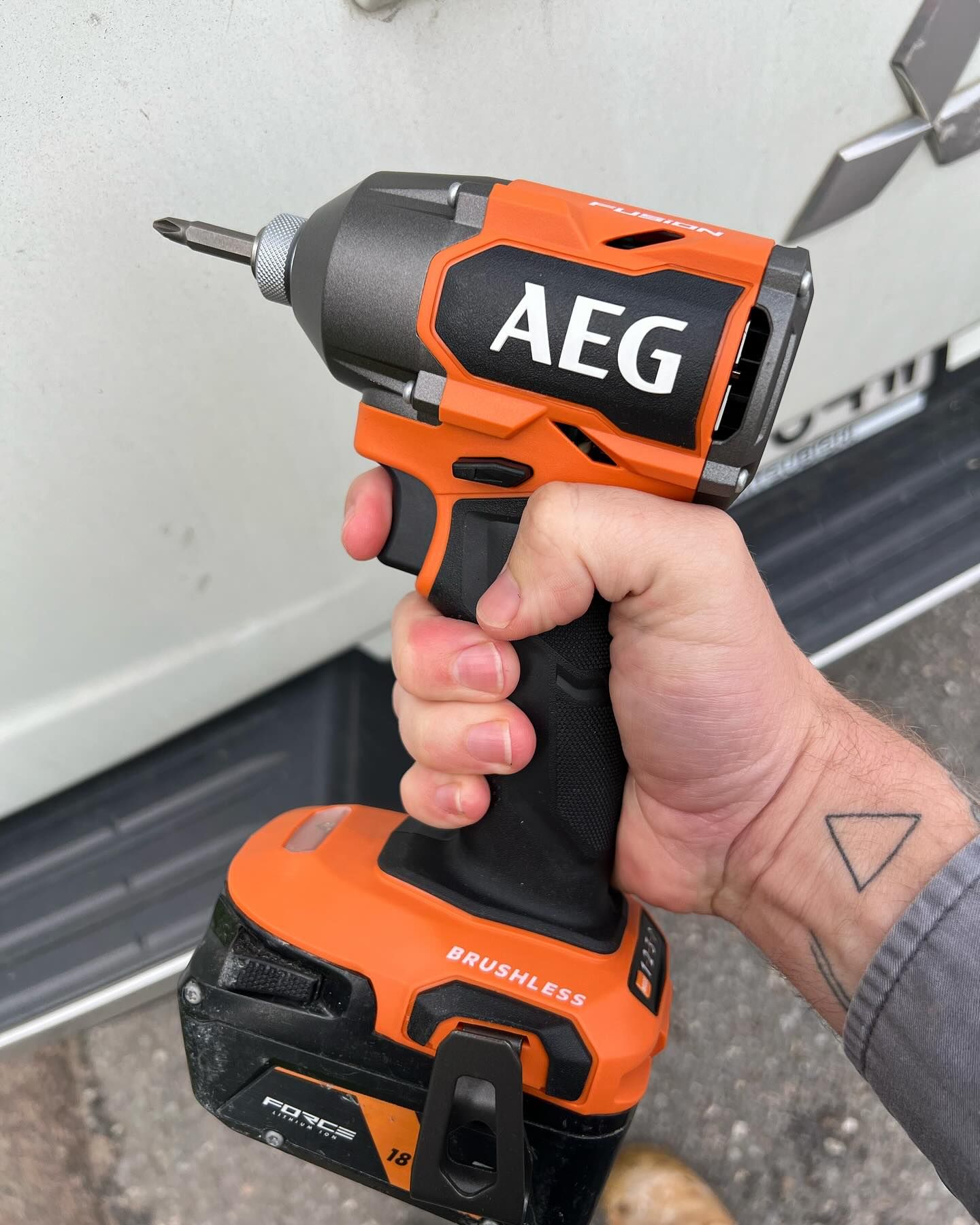 Hand Holding an Orange and Black AEG Impact Driver — Hunter Fire & Safety in Edgeworth, NSW