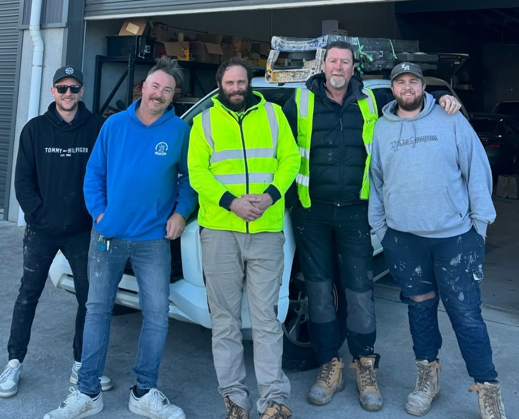 Five People Stand in Front of a White Car in a Garage — Hunter Fire & Safety in Edgeworth, NSW
