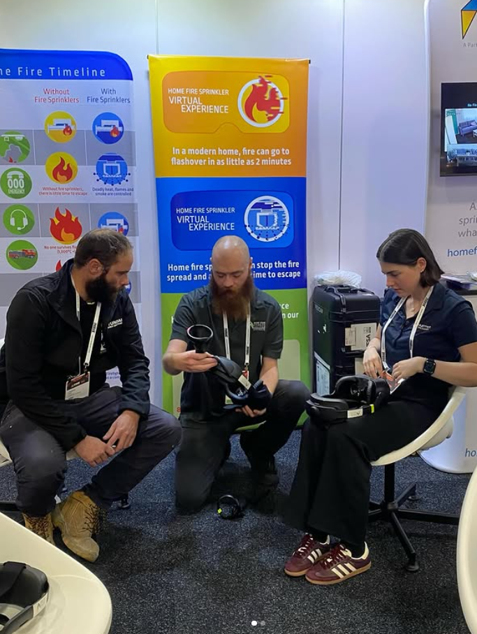 Three People at a Booth, One Kneeling With Vr Headset — Hunter Fire & Safety in Edgeworth, NSW