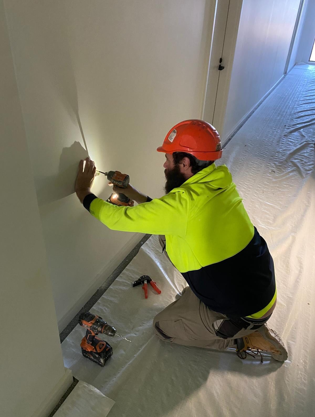 A Construction Worker Using a Drill on a Wall — Hunter Fire & Safety in Edgeworth, NSW