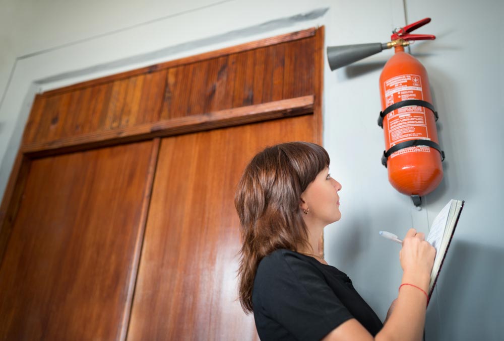 Woman Inspecting a Fire Extinguisher Near Wooden Doors — Hunter Fire & Safety in Edgeworth, NSW