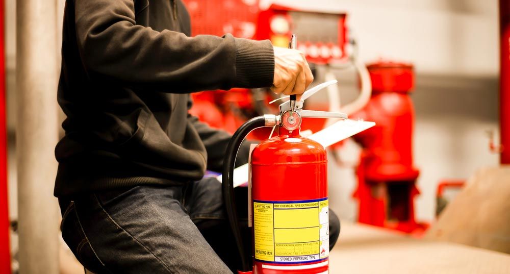 Person in Black Sweater Holding a Red Fire Extinguisher — Hunter Fire & Safety in Edgeworth, NSW