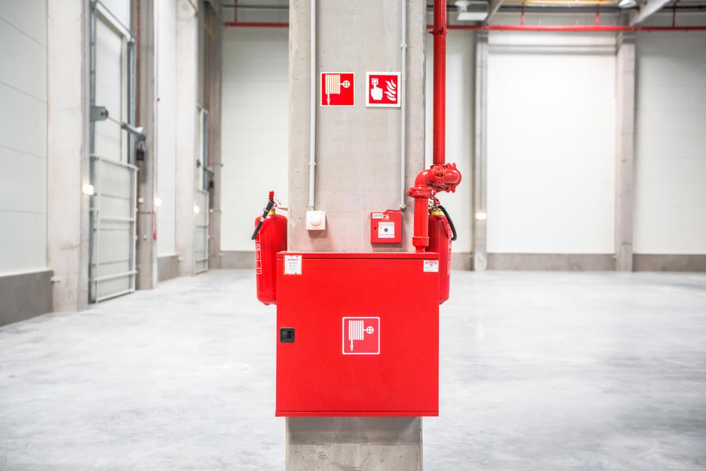 Red Fire Safety Equipment on a Concrete Pillar in a Large, Empty Warehouse — Hunter Fire & Safety in Edgeworth, NSW