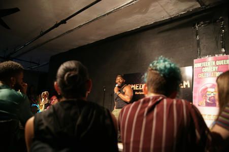 Audience watching a comedian perform on a small stage in a dimly lit venue
