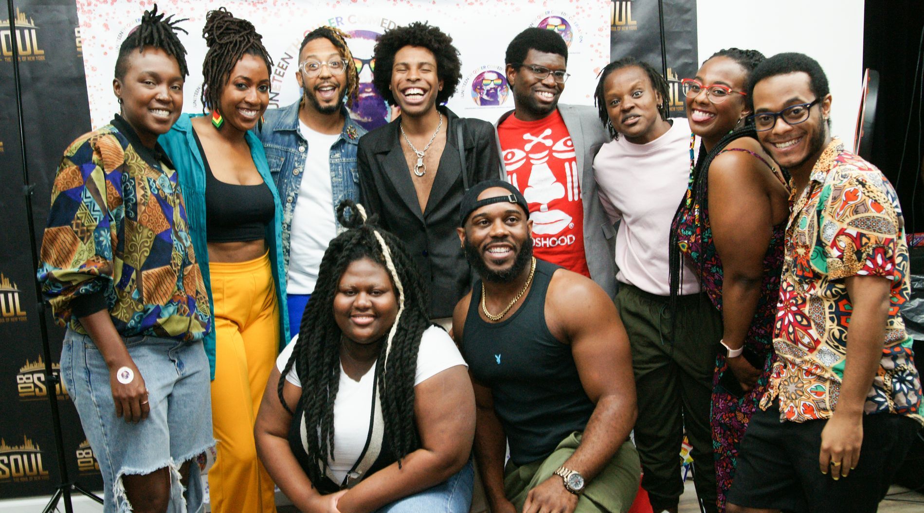 Group of eight people posing together indoors, smiling in front of a branded backdrop.