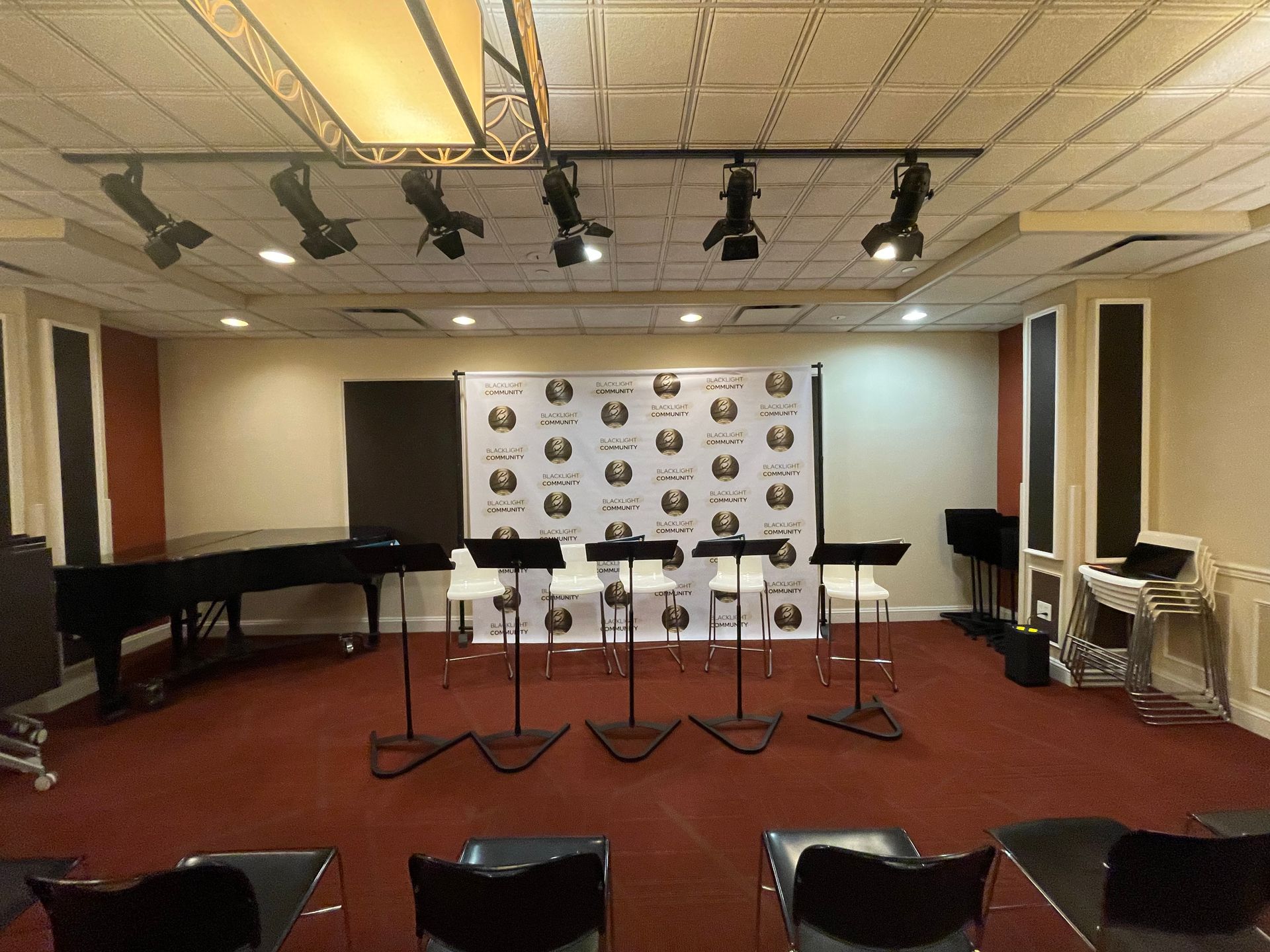 Empty press conference stage with microphones, grand pianos, and a backdrop in a room with red carpet and ceiling lights