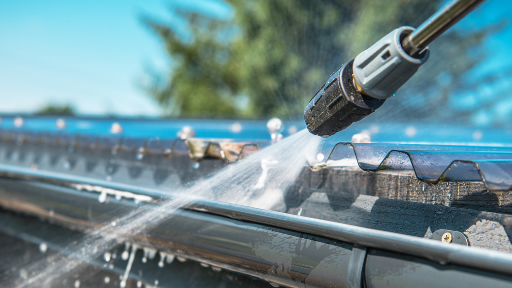 Pressure washer cleaning a dark gutter on a sunny day.