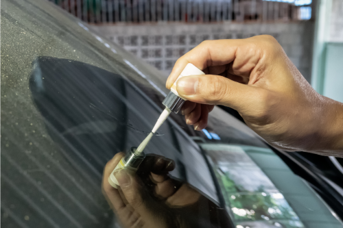 A person trying to repair a small windshield crack with a tool