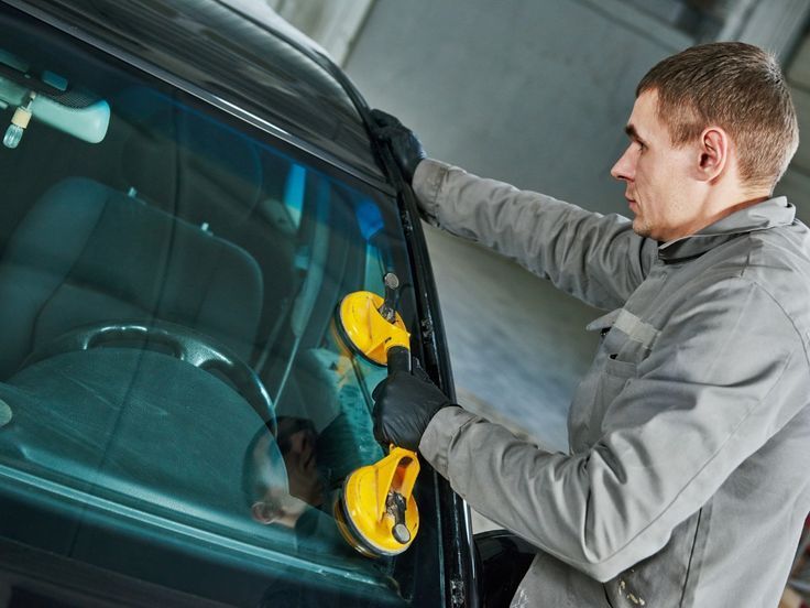 Technician using a yellow suction-cup tool to repair a car windshield in a garage