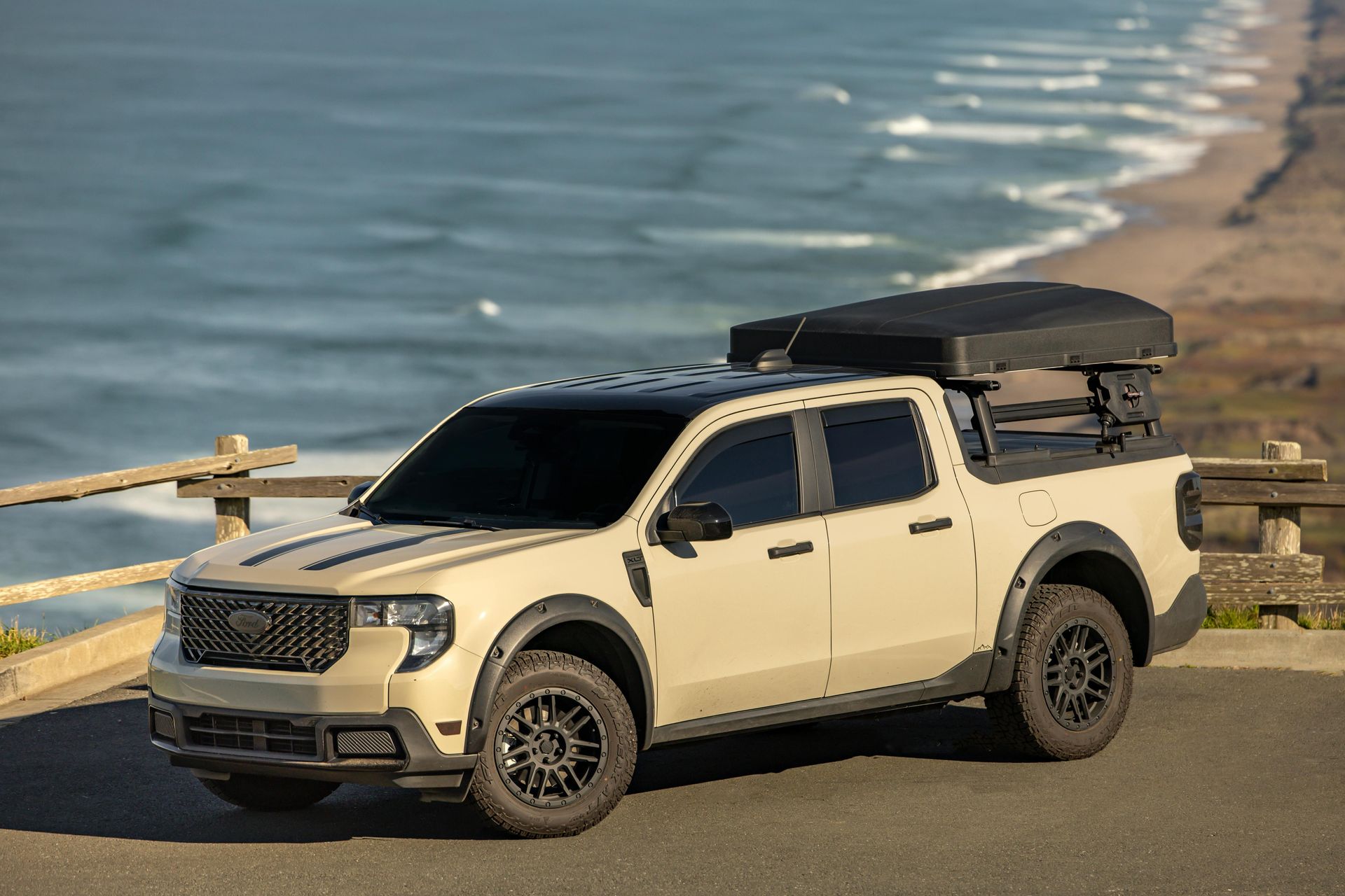 Tan Ford pickup truck with a black roof rack, parked near the ocean.
