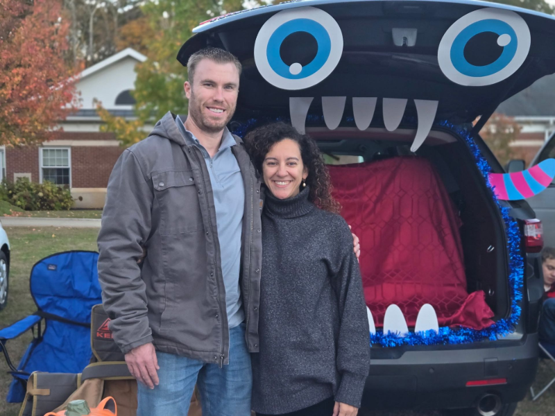 Smiling couple posing beside a decorated car with a monster face trunk display outdoors