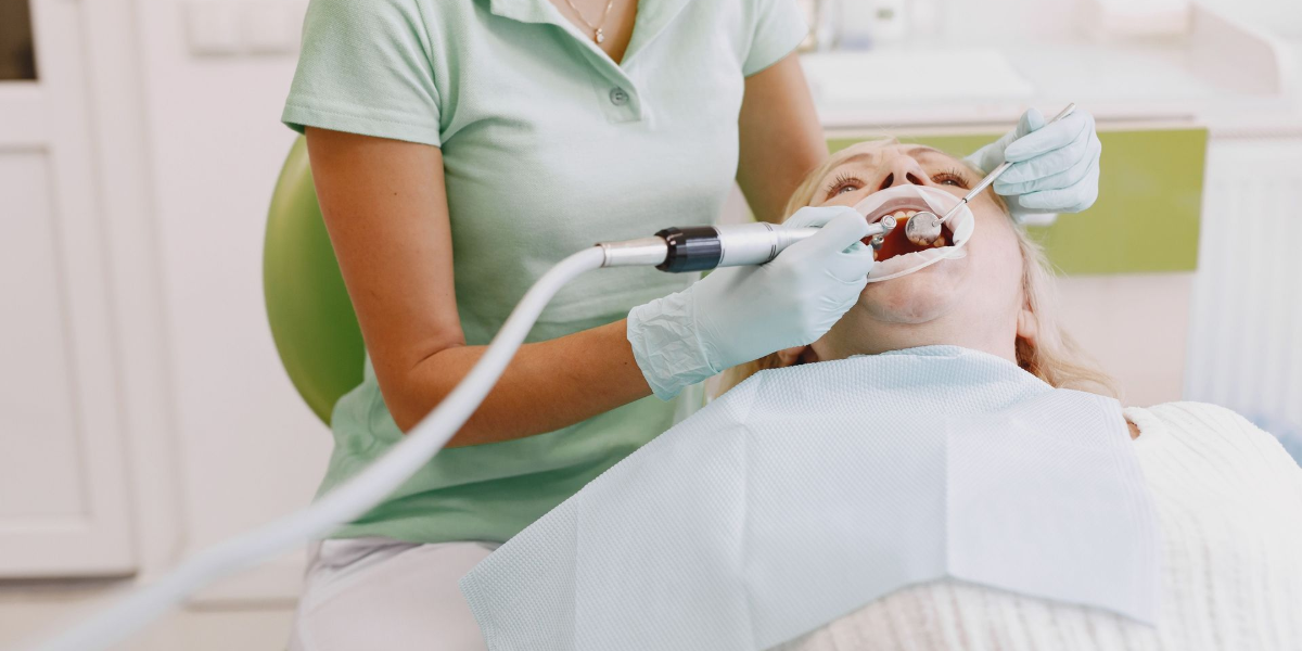 Dentist using a drill on a patient in a dental chair, wearing gloves and a green uniform