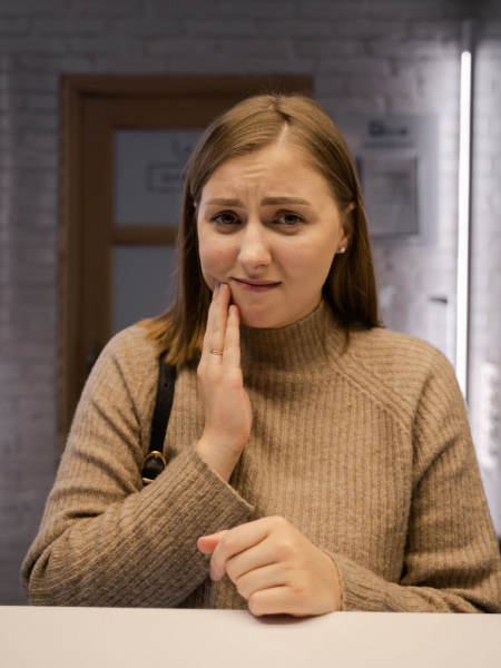 Woman touching her cheek with a concerned expression at a kitchen table