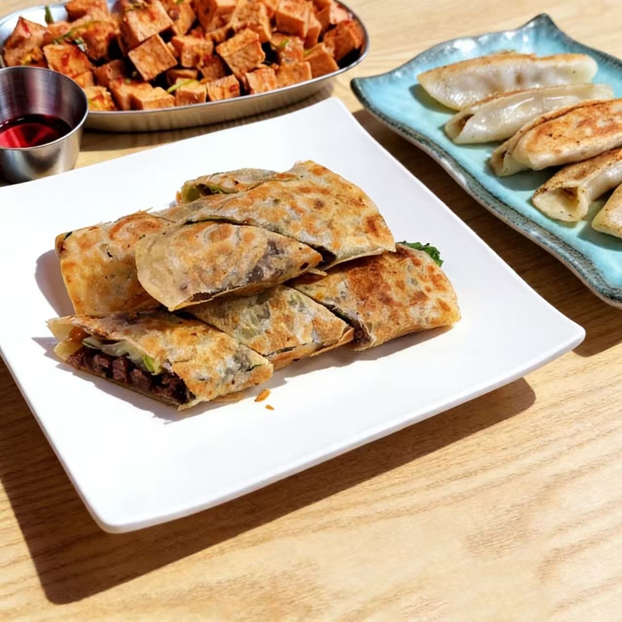 Plates of assorted Asian appetizers: fried rolls, stuffed flatbreads, and cubes with dipping sauce on a wooden table