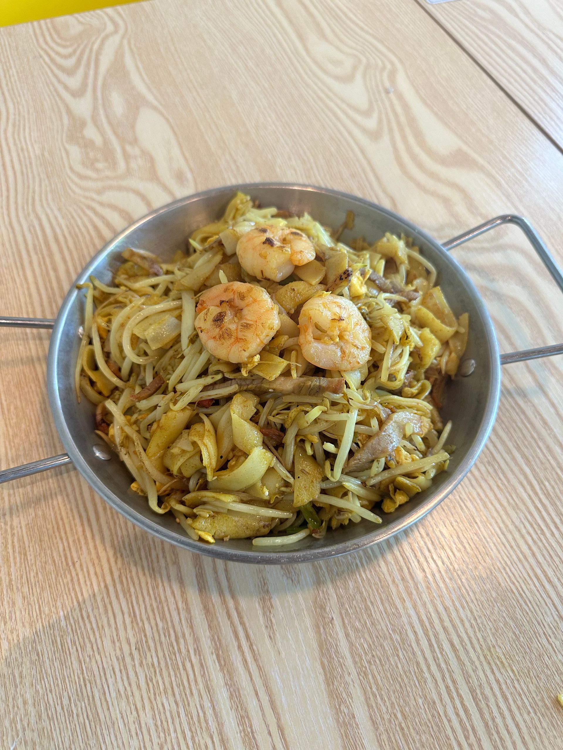 Bowl of stir-fried noodles with shrimp on a light wooden table