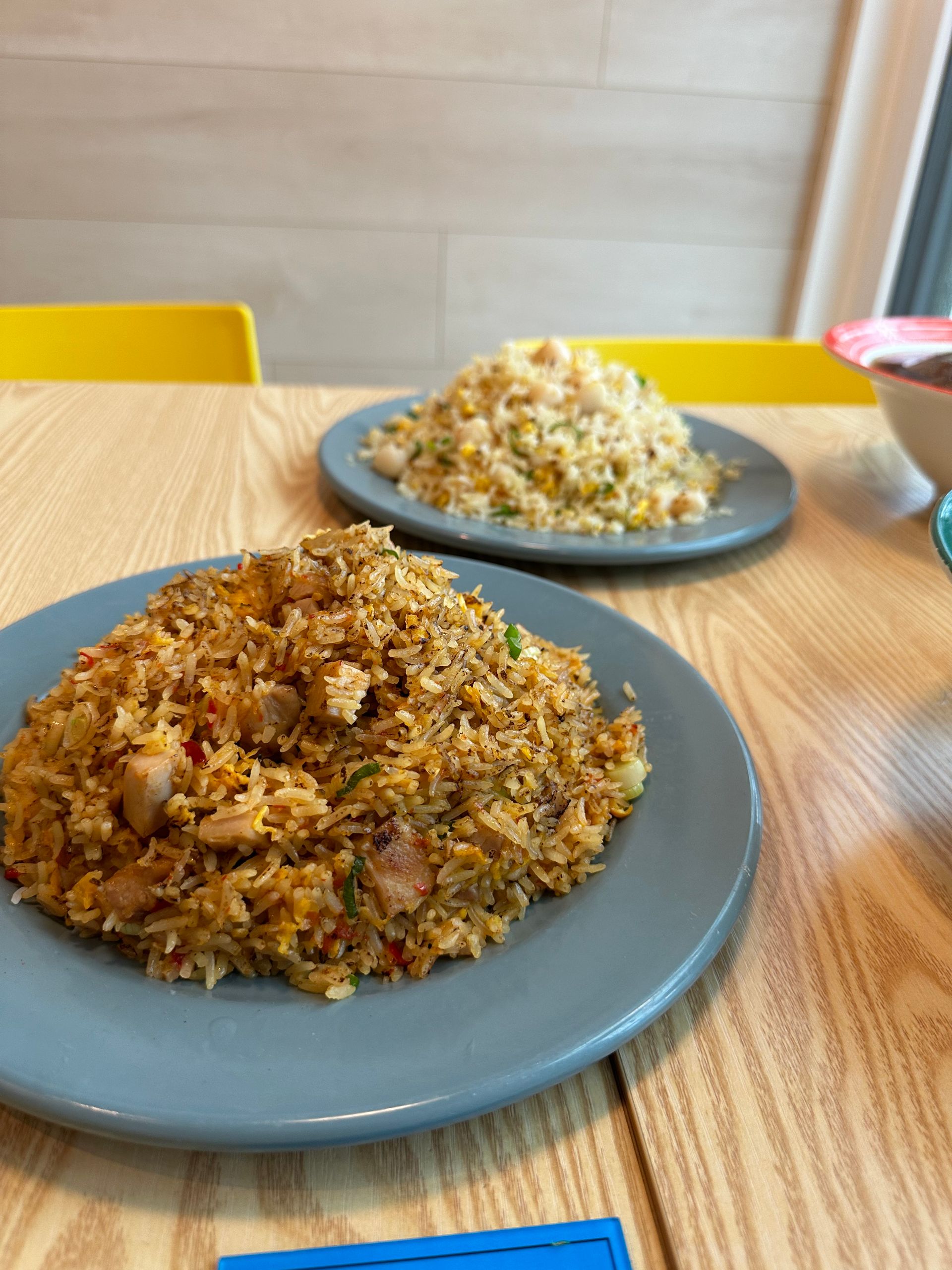 Two plates of fried rice on a wooden table with yellow chairs in the background