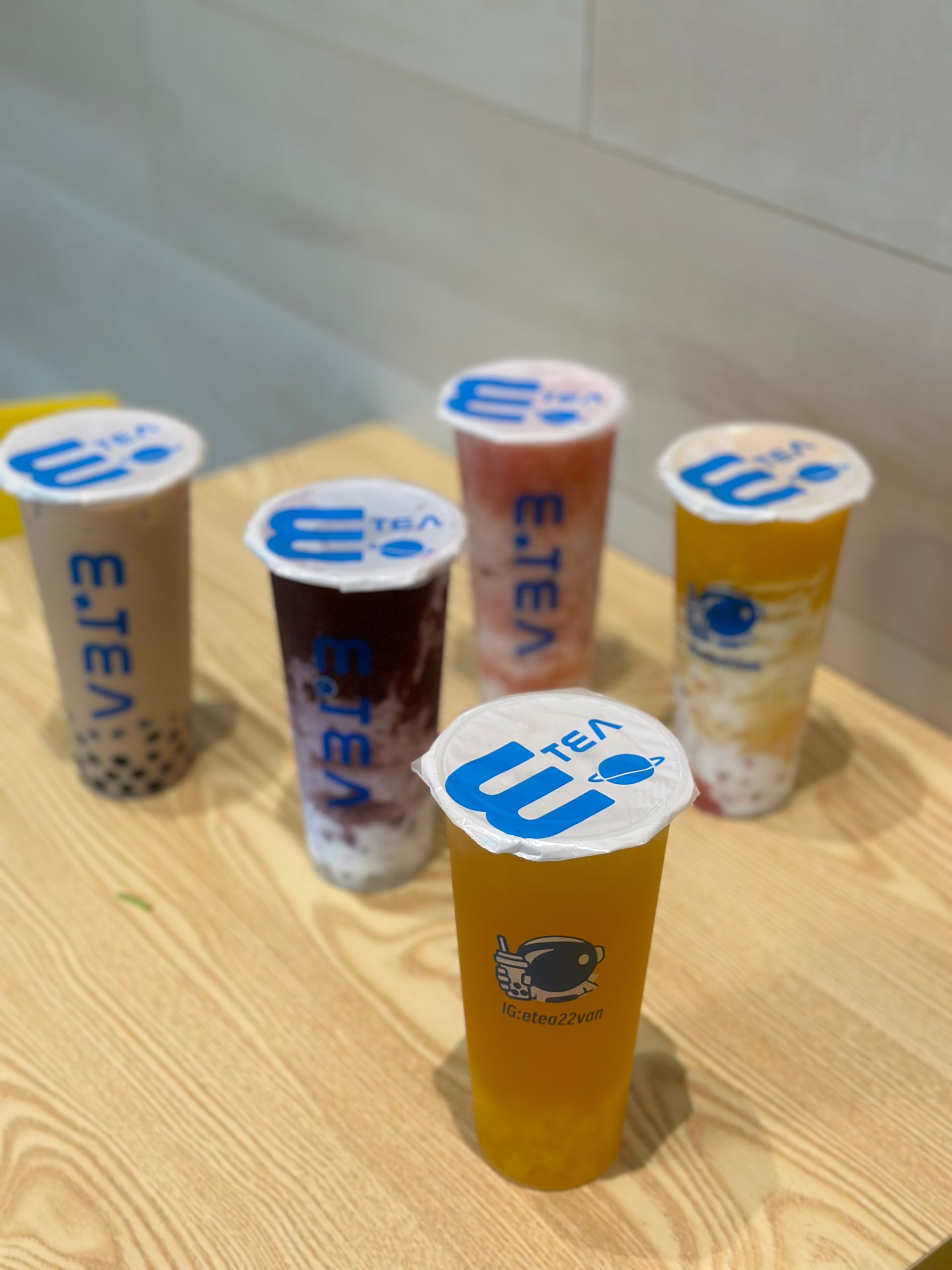 Five yogurt cups on a wooden table, one in front with a yellow label and four behind it.