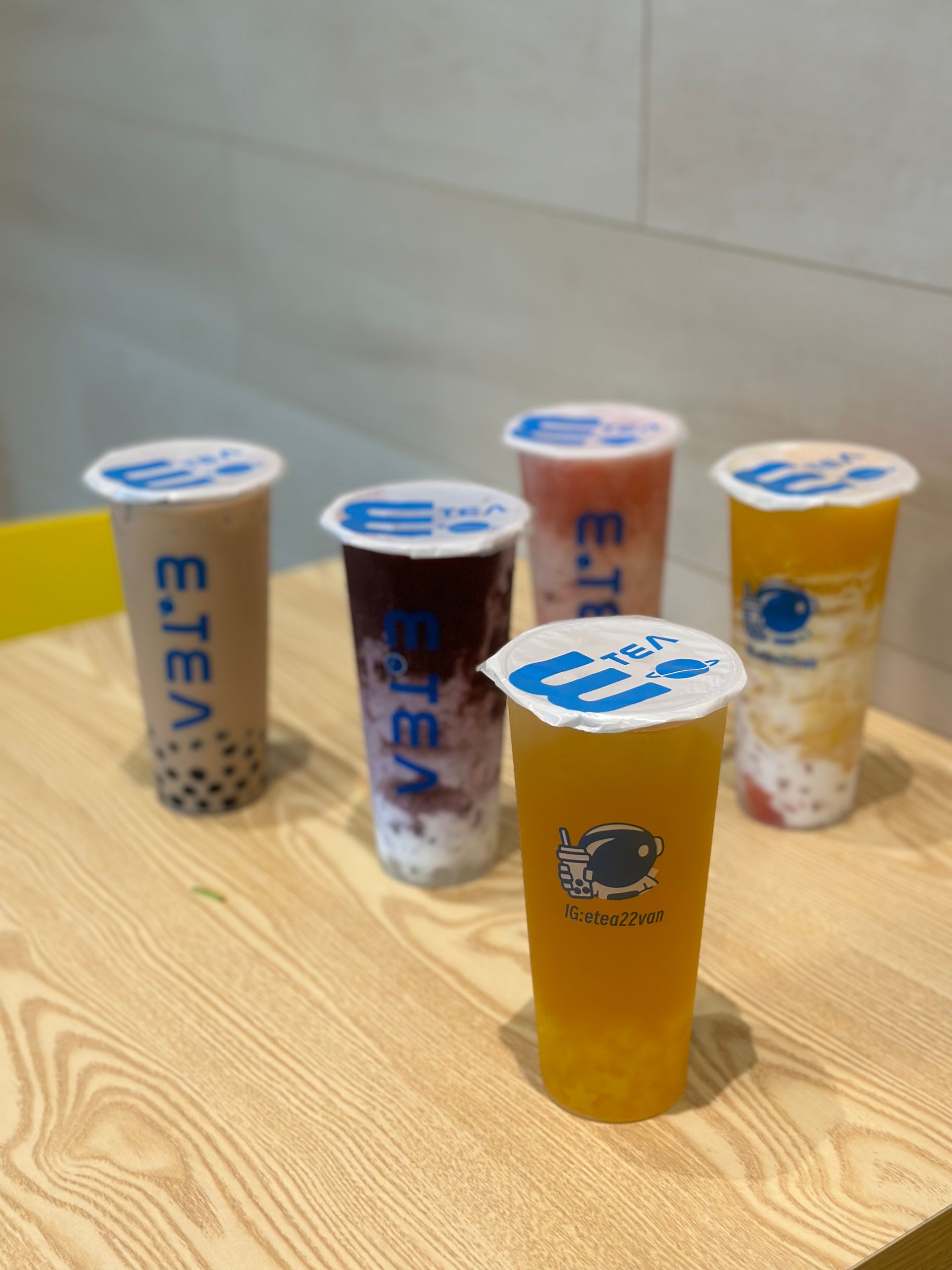Four branded drink cups with lids on a wooden table, including one amber-colored cup in the foreground.