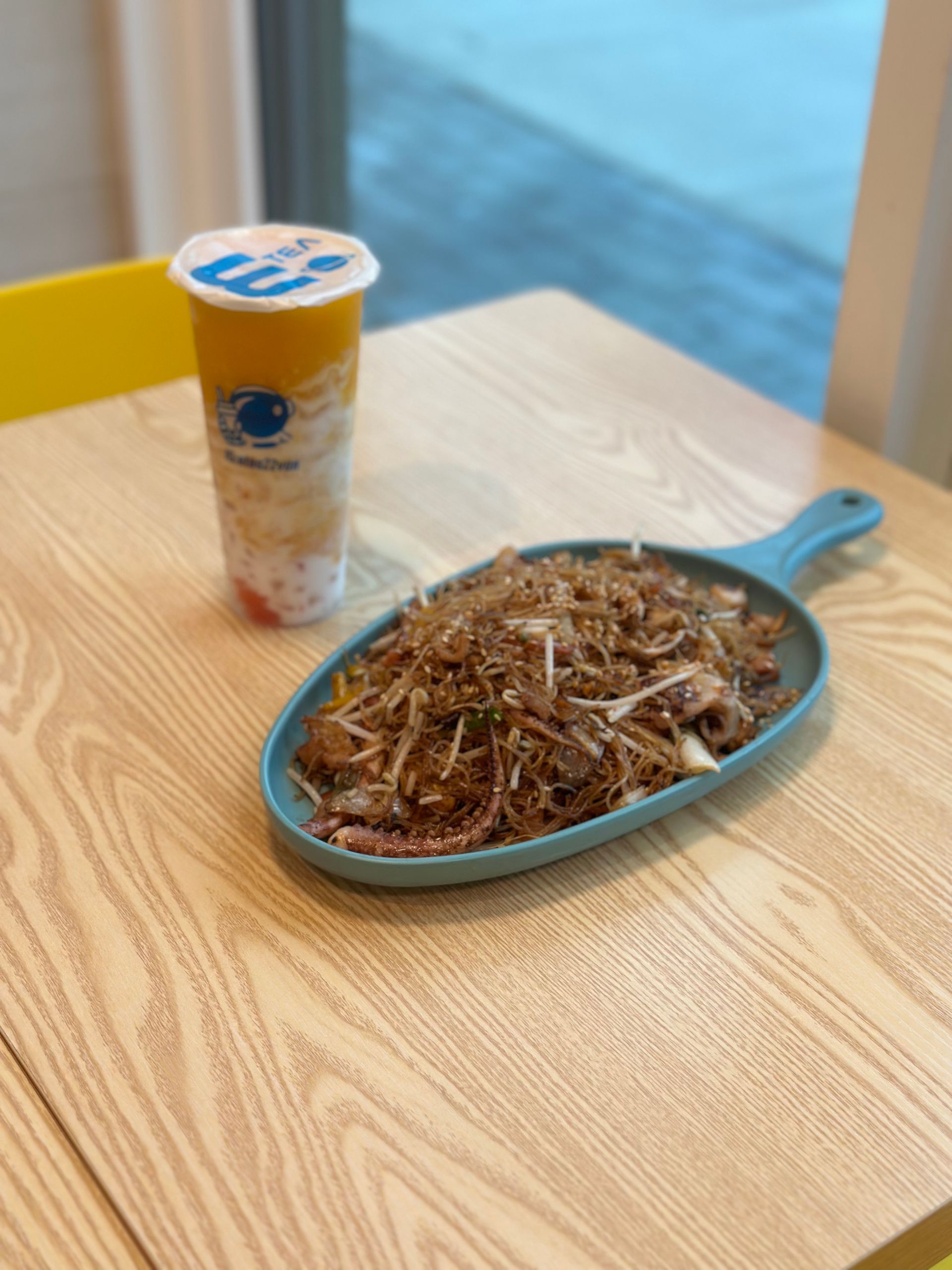 Blue dish of shredded food beside a yellow drink cup on a wooden table