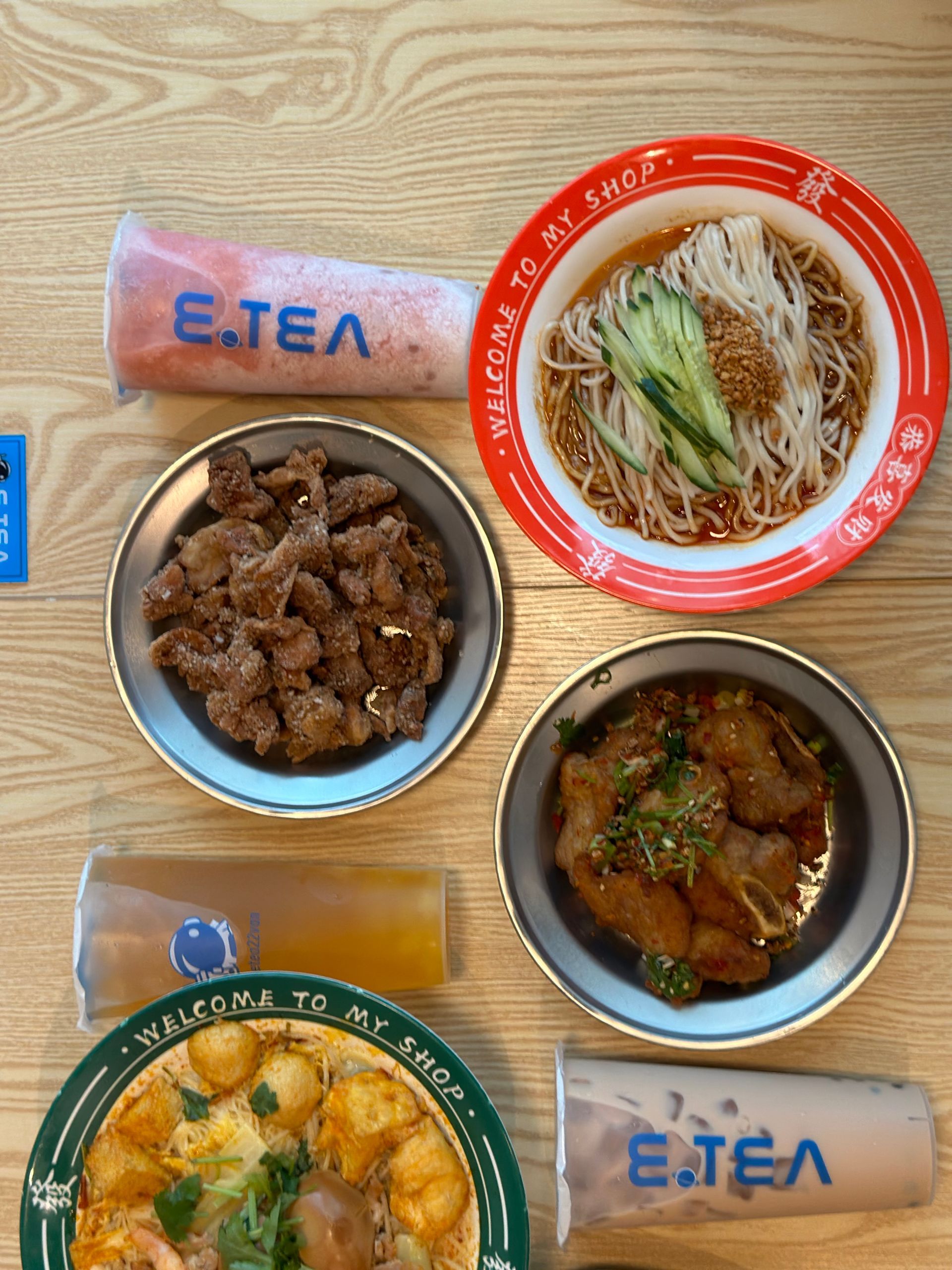 Assorted Korean meal with noodle soup, rice dishes, meat, and packaged wet wipes on a wooden table.