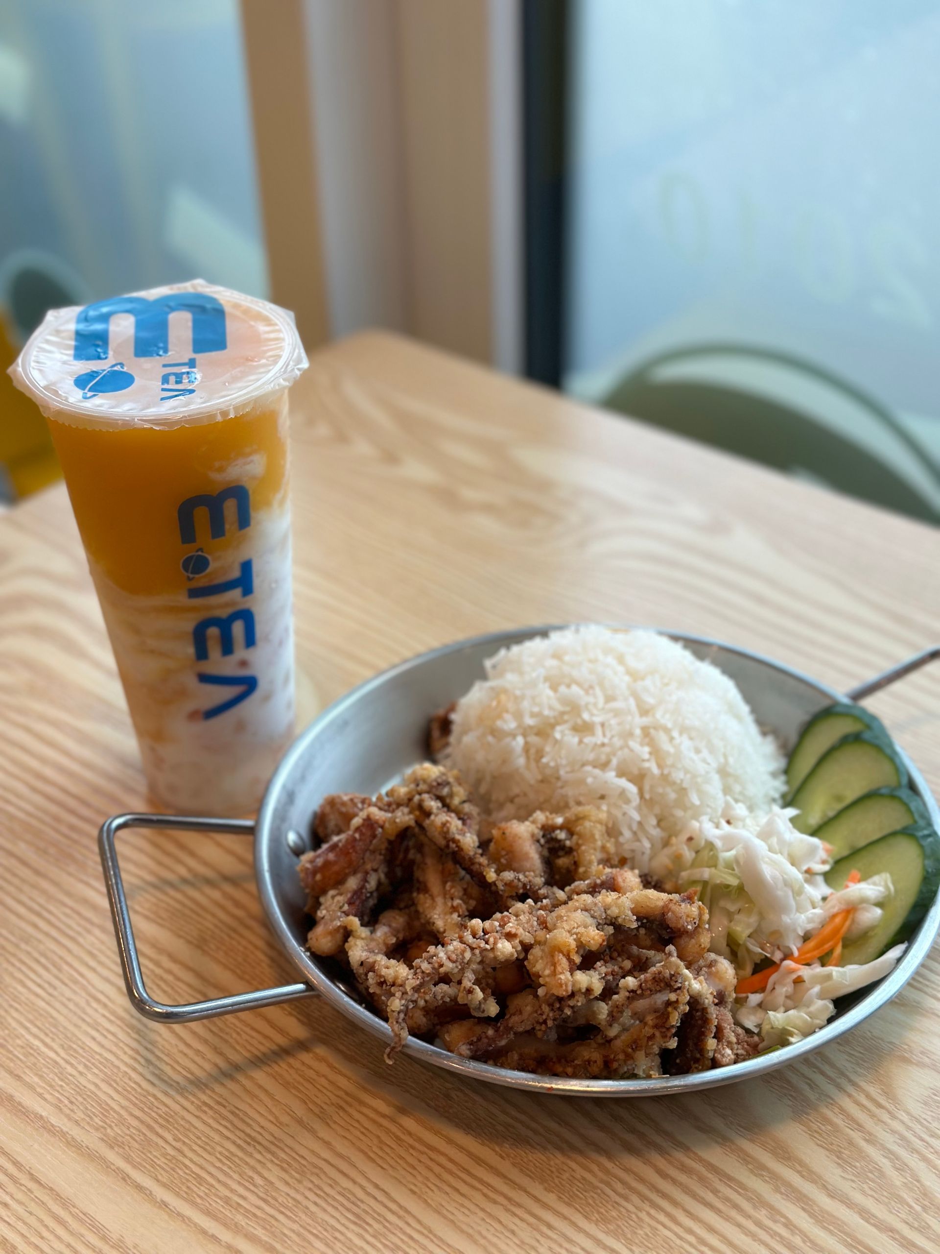 Rice bowl with stir-fried meat, cucumber slices, and a milk drink on a wooden table.