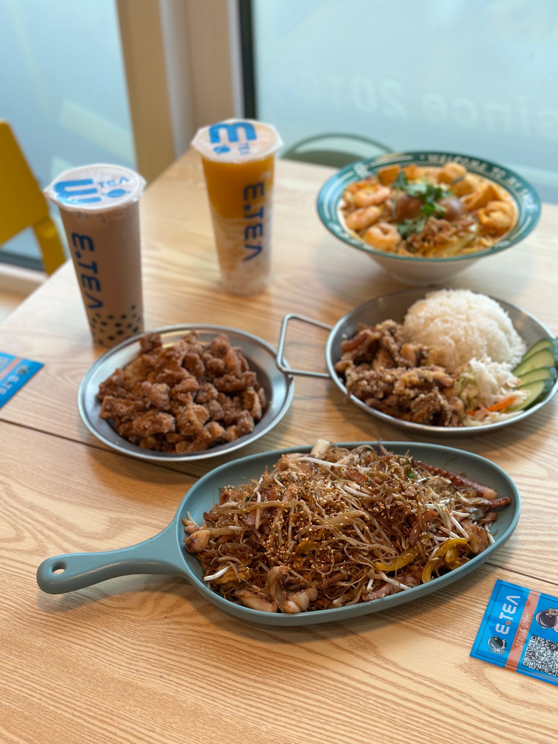 A table with several bowls of food and two drinks on a wooden tray.