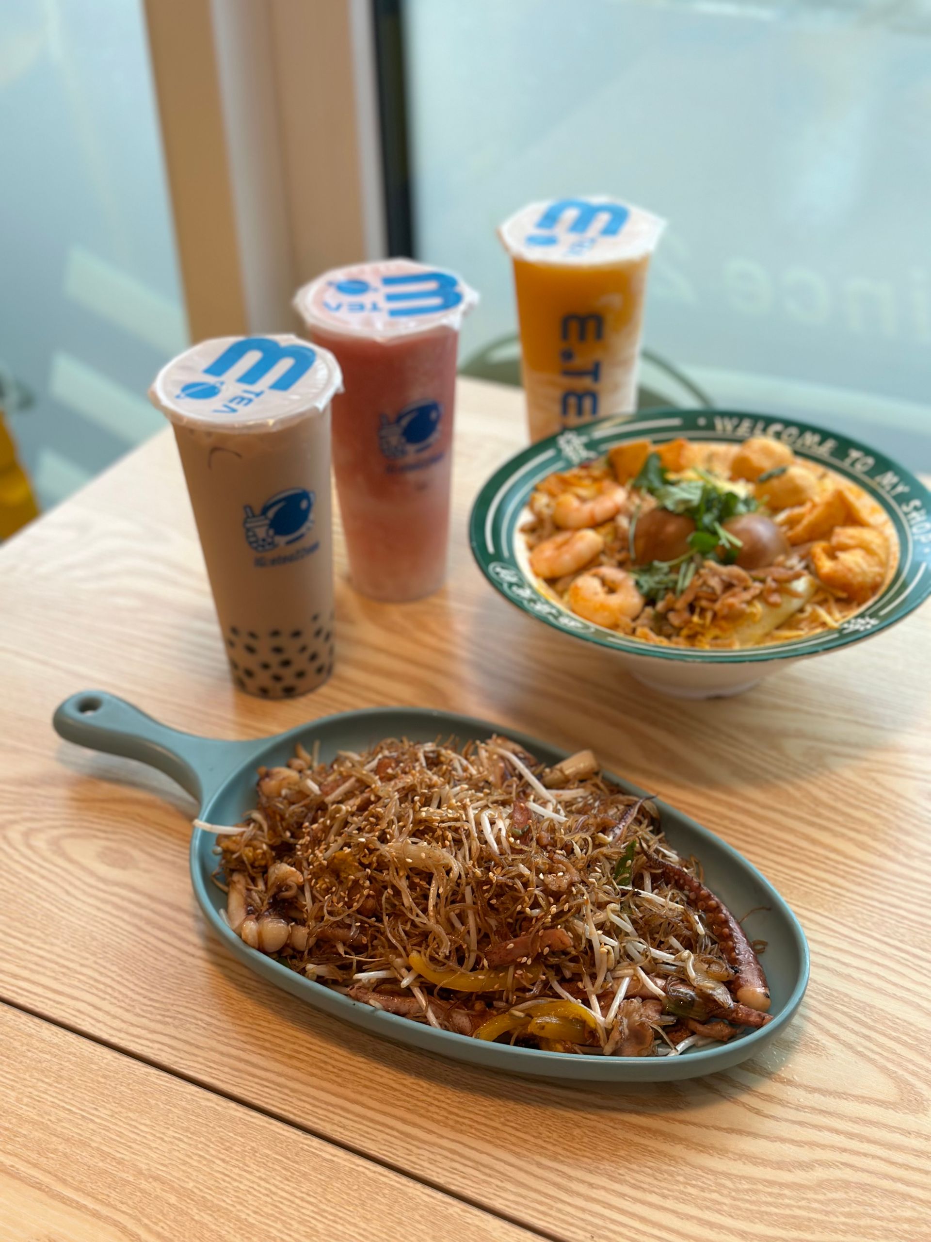 Table with three bubble teas and two dishes of food on a wooden surface