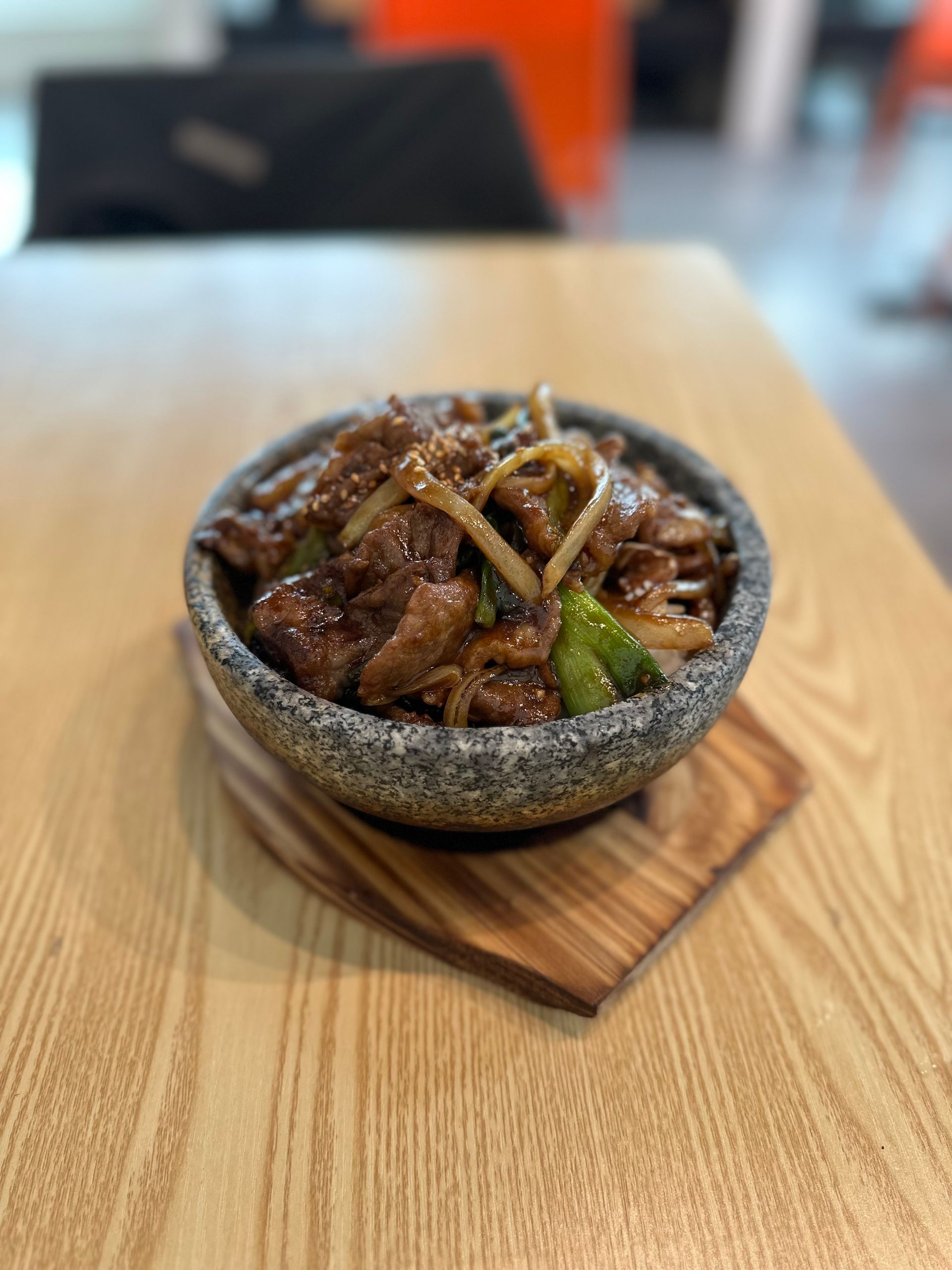 Stone bowl of glazed meat and vegetables on a wooden tray at a restaurant table