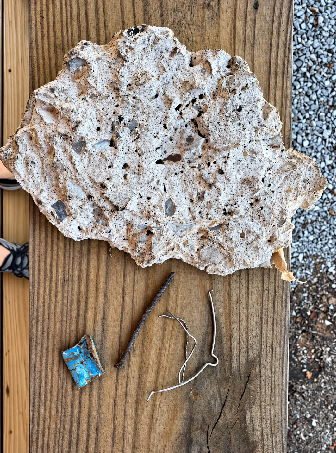 Large white porous rock on wood decking, with small blue trash and a wire nearby.
