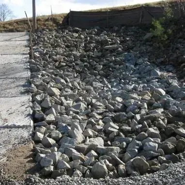 Rock-covered drainage ditch beside a paved road under a cloudy sky