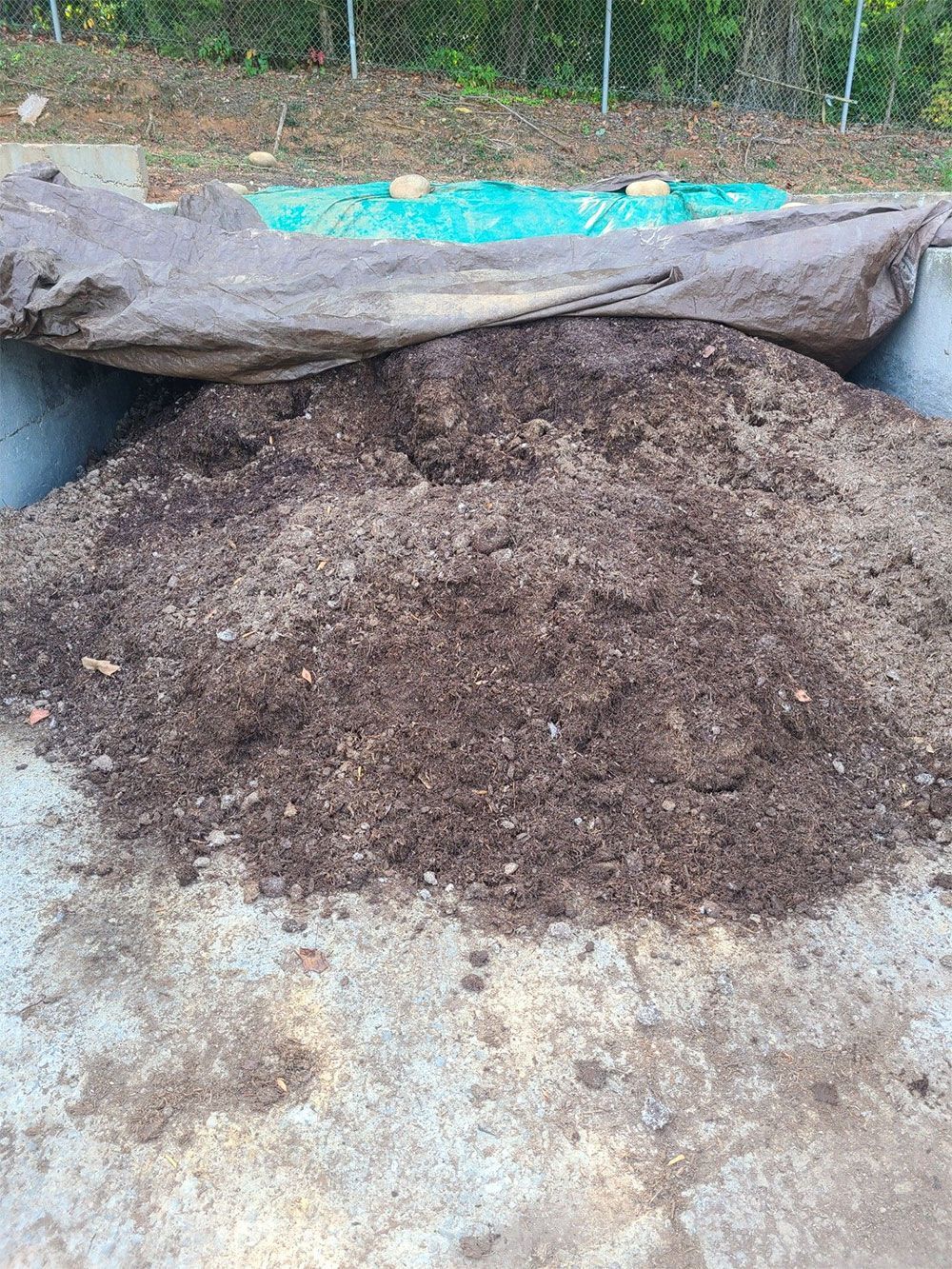 Large pile of dark brown compost or mulch beside a covered mound outdoors.