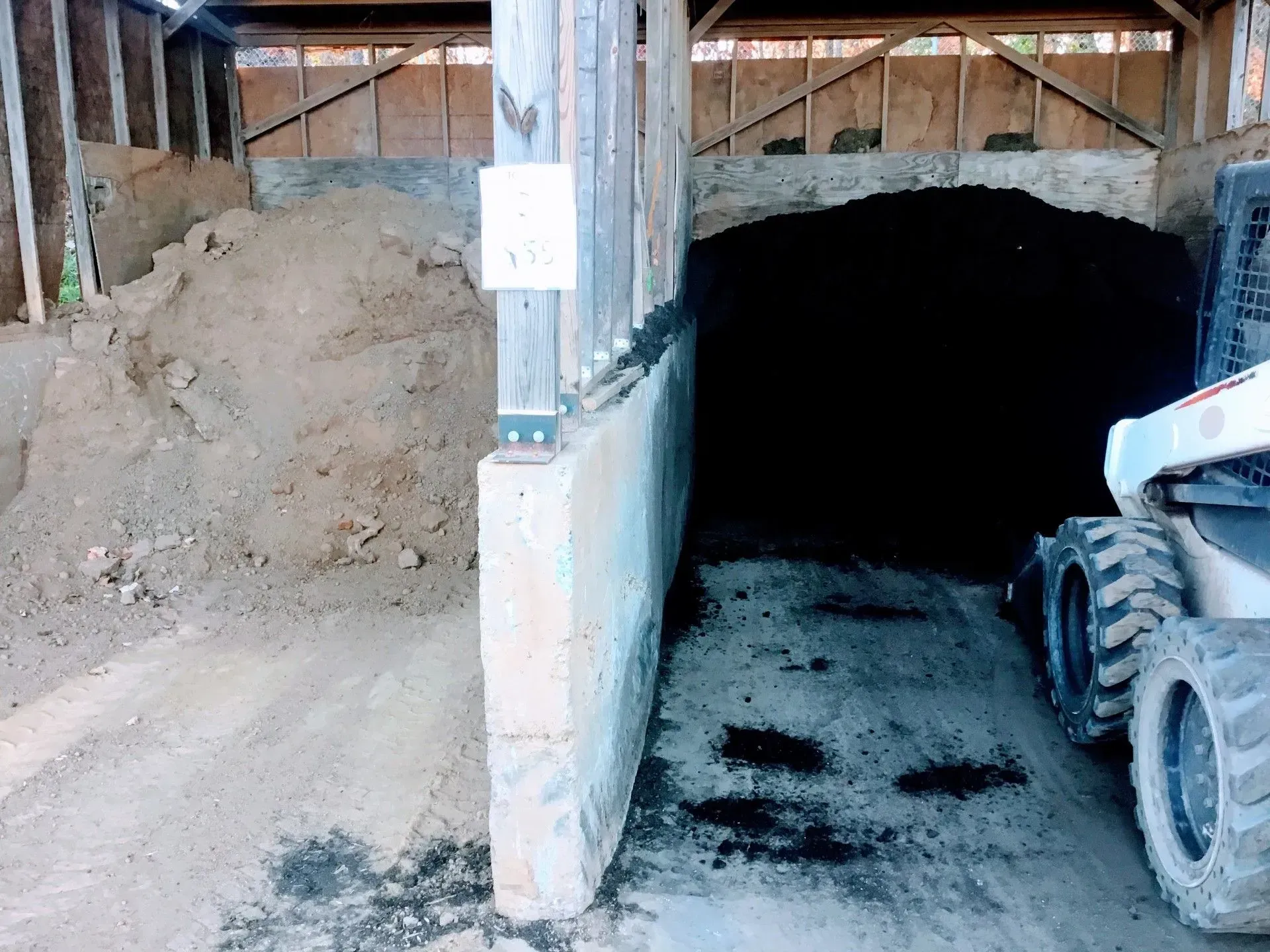 Construction site interior with a wheel loader beside a dark tunnel entrance and dirt pile