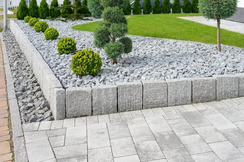 Landscaped stone garden with gray gravel, trimmed shrubs, and paved walkway