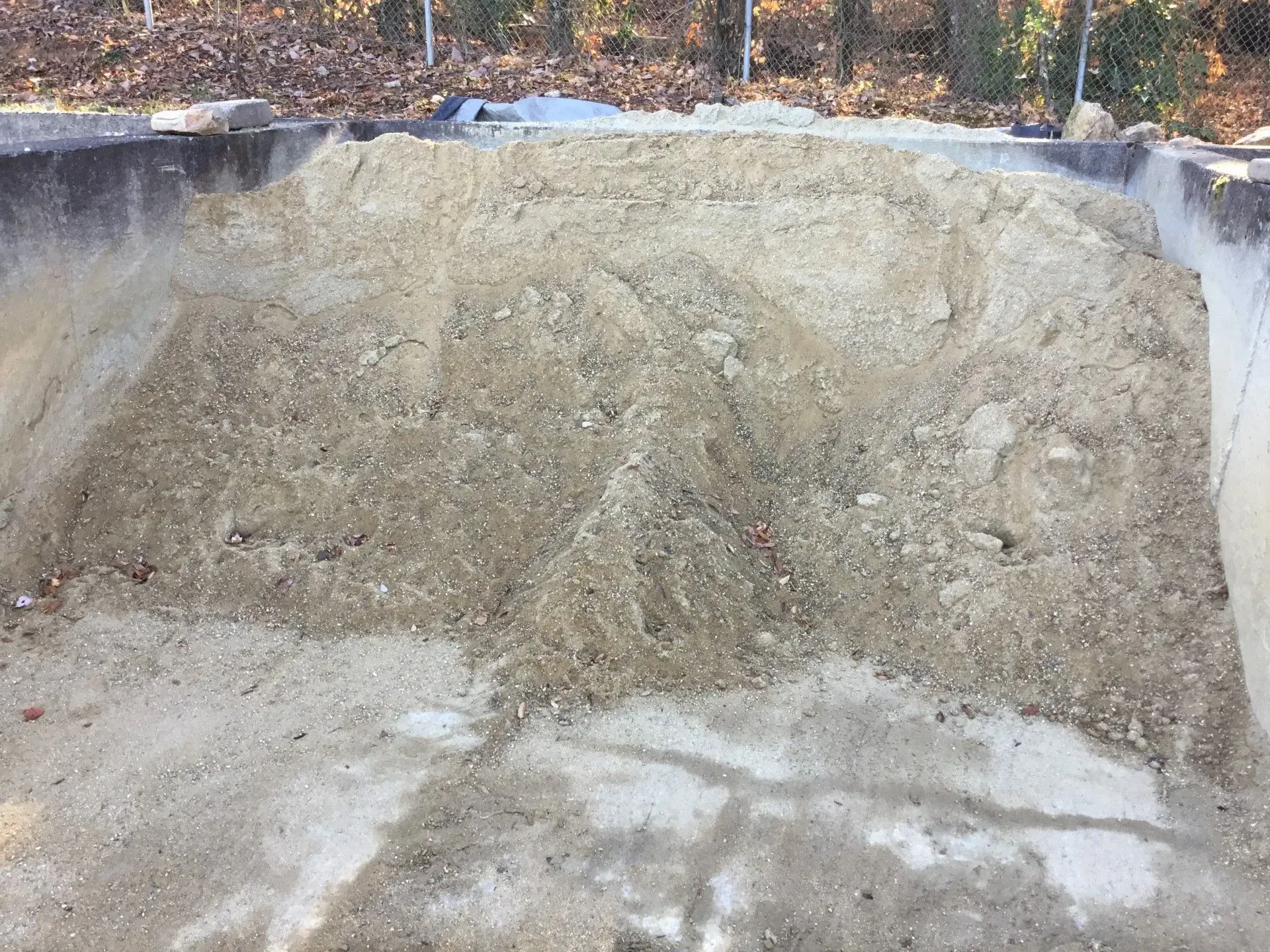 Dirt excavation pit with steep sandy walls and a wooded edge at the top