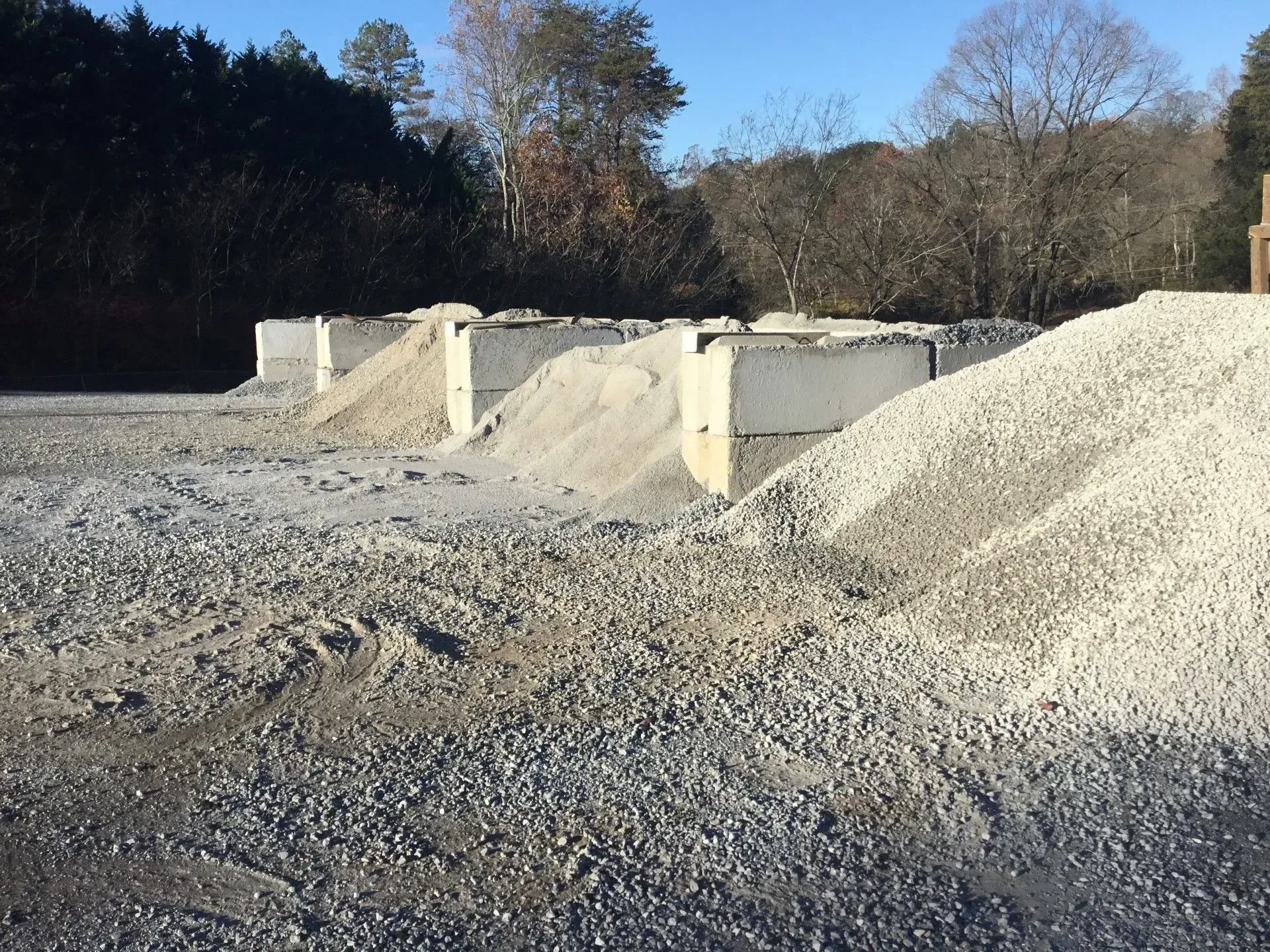 Gravel quarry with large piles of crushed stone and concrete barriers under a clear blue sky