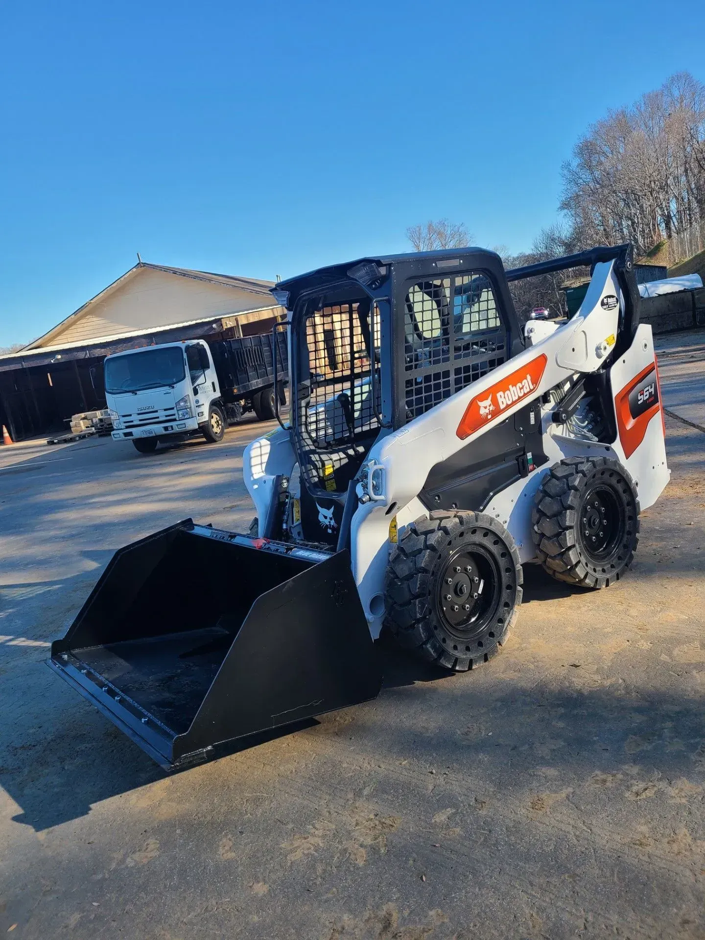 White-and-black skid-steer loader with bucket on a driveway in front of a house and garage.