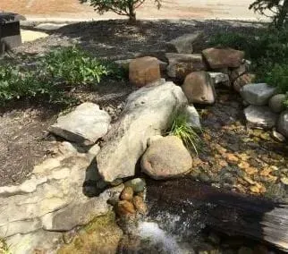 Rock garden with a small water stream flowing over tan stones and rocks in a landscaped yard