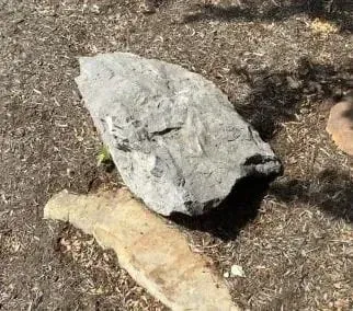 Two rocks on dry ground, one large gray and one smaller tan, in sunlight