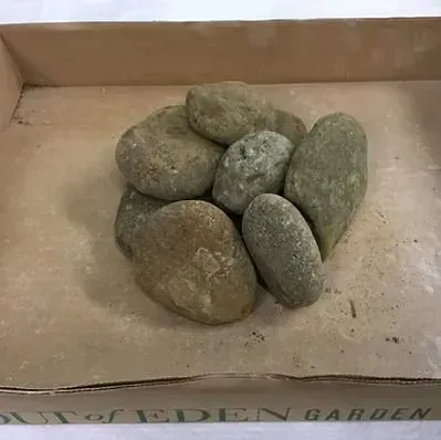 Stack of six smooth gray-green stones in a cardboard box on a dusty surface