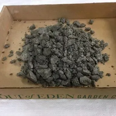 A cardboard box filled with a pile of gray rocks or gravel on a tan surface.
