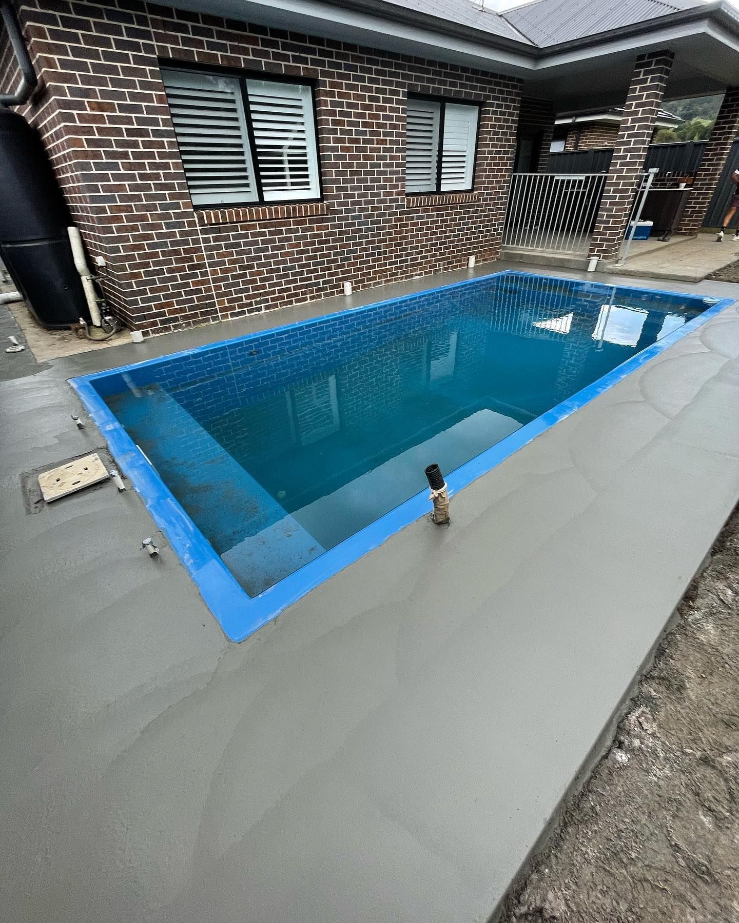A Rectangular Swimming Pool With Blue Water Sits in a Newly Paved Concrete — JDB Concreting in Horsley, NSW