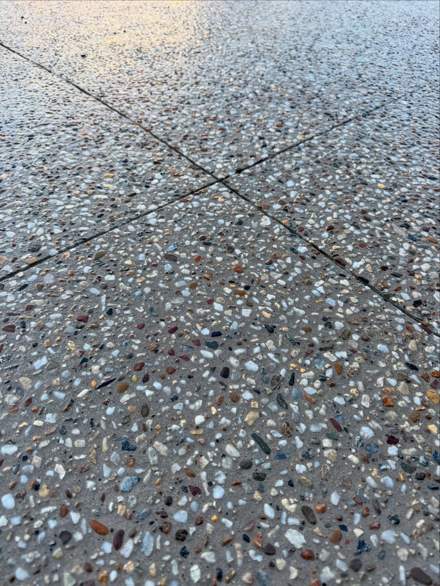 A close-up view of a gray concrete surface with exposed multi-colored aggregate stones and intersecting joint lines. — JDB Concreting in Dapto, NSW