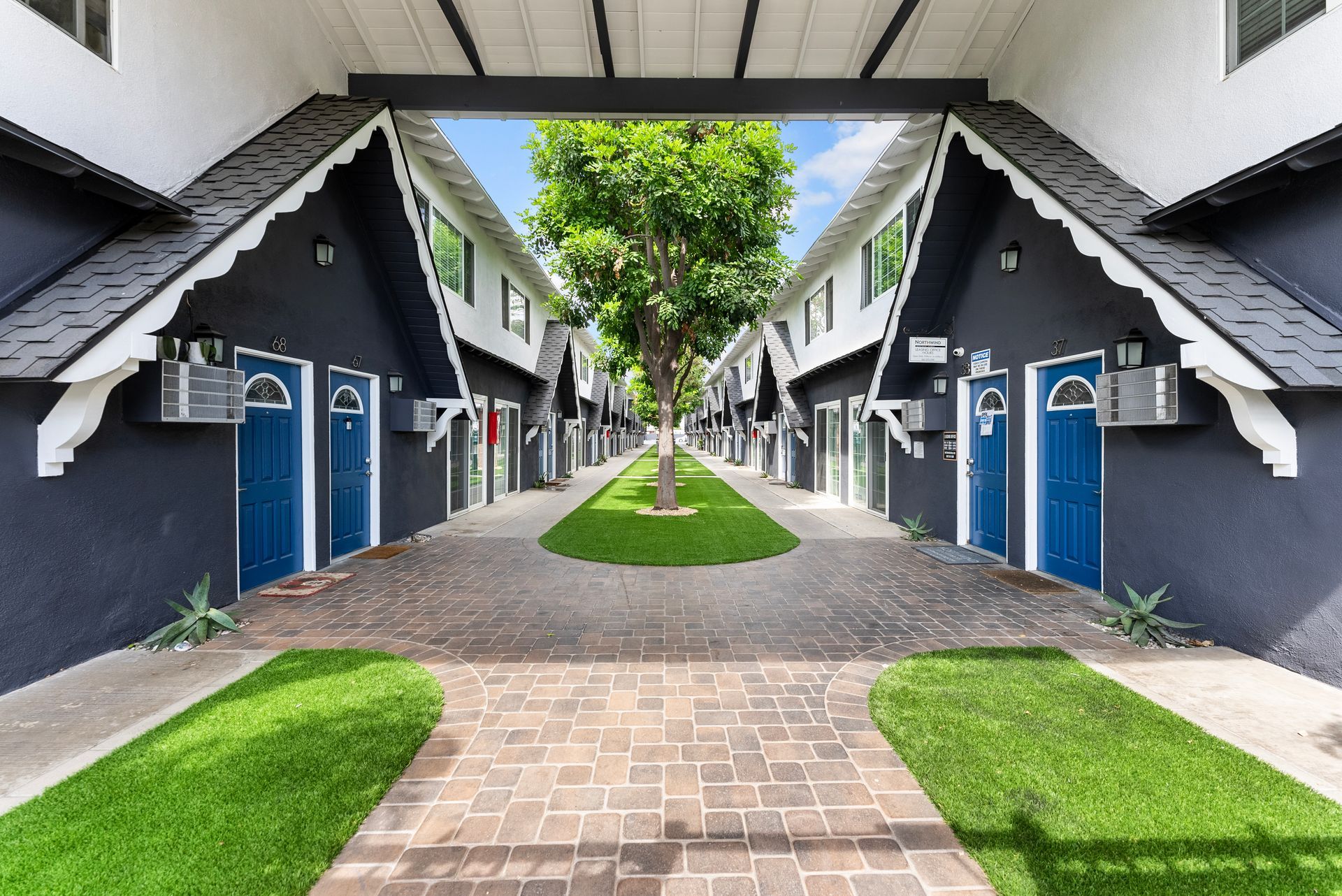 Exterior walkway of Northwind with grass patch, gray triangular archway, and two blue front doors.